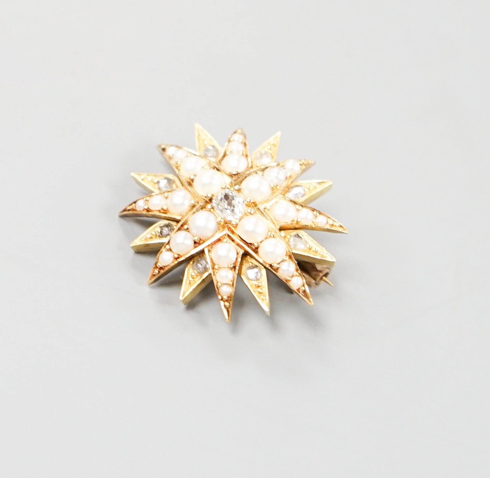 An Edwardian yellow metal, graduated split pearl and single stone diamond set starburst brooch(adapted?), 24mm, gross weight 6.5 grams.